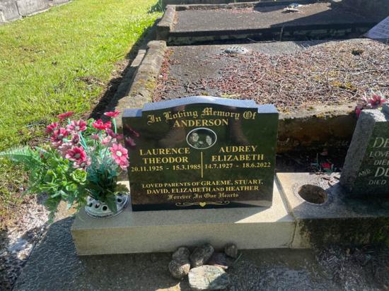 Classic upright headstone with a high saddle with checks shape, crafted from polished granite. This is a companion headstone for a husband and wife, and includes a photo. by Mark Memorials in Levin, New Zealand.