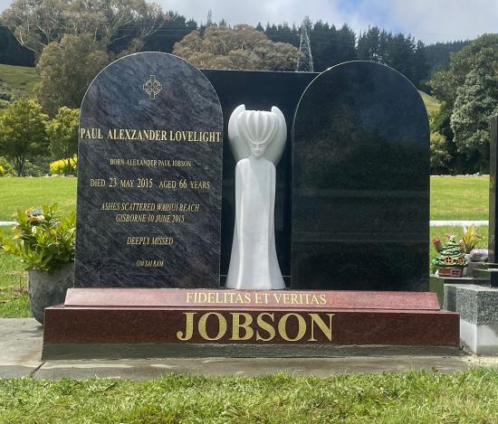 Double upright headstone with round top, crafted from polished granite. A white carved figure contrasts with the black granite.  By Mark Memorials in Levin, New Zealand.