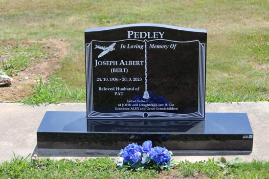 Classic upright headstone with low saddle top and a book engraving, crafted from polished granite. This is a double or companion memorial, leaving space for the second person.  By Mark Memorials in Levin, New Zealand